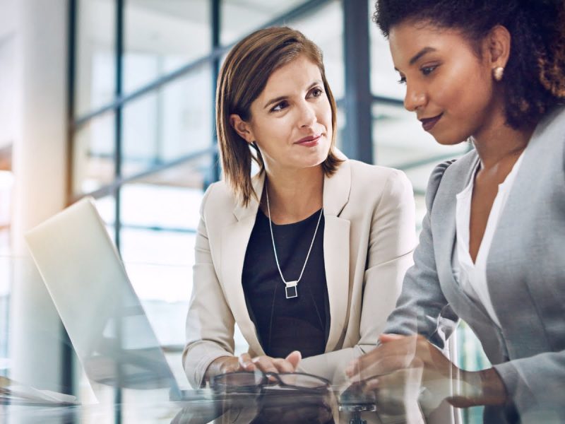 Two business women programming on a laptop in an office discussing the Freshealth Select Program for brokers.