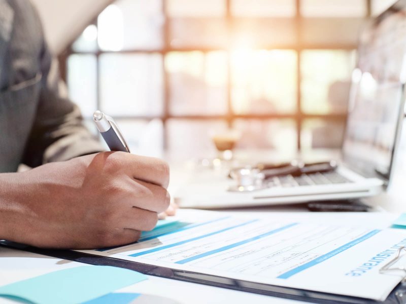 A businessman signing a document in front of a laptop.